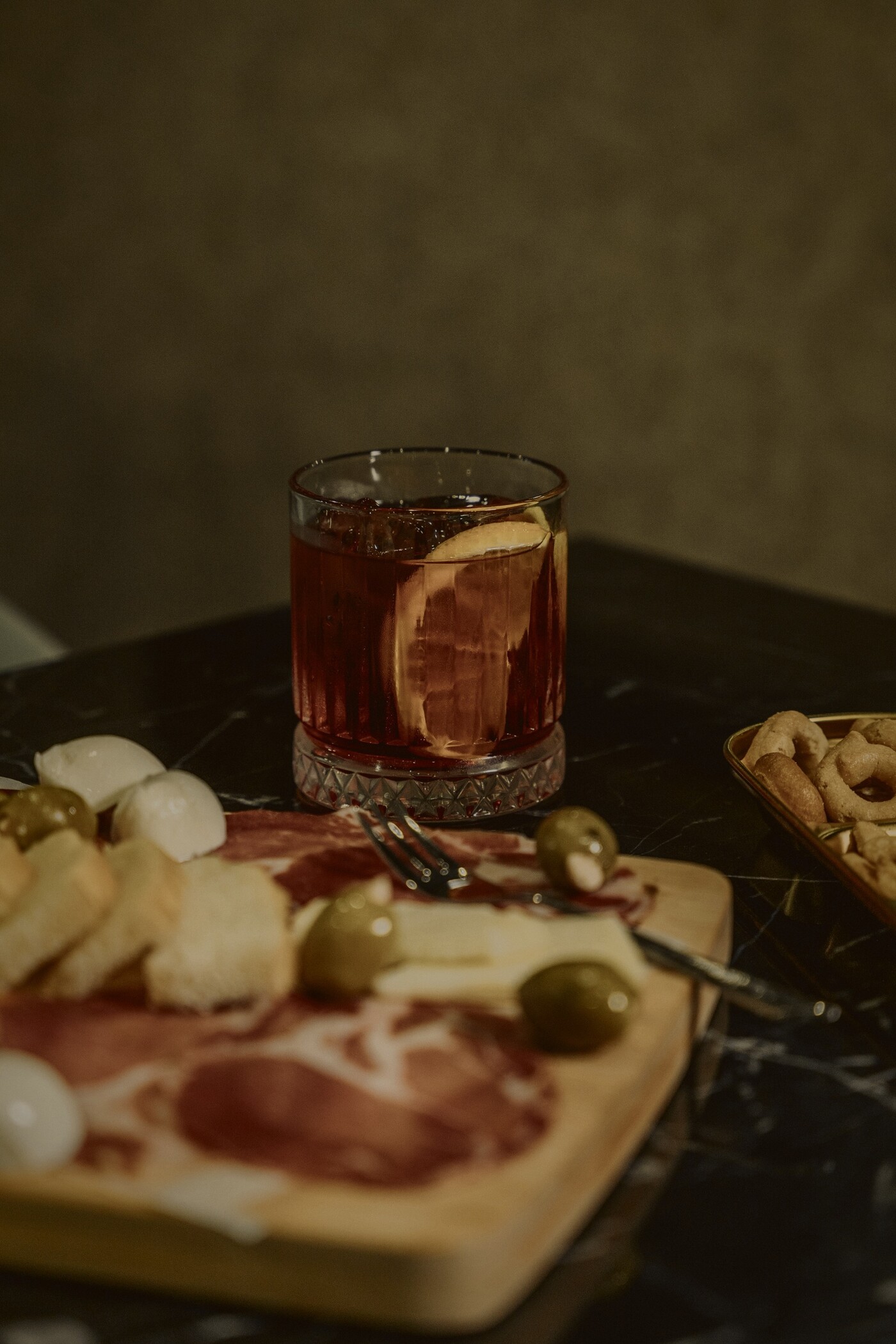 Negroni junto a una tabla de jamón, queso y aceitunas